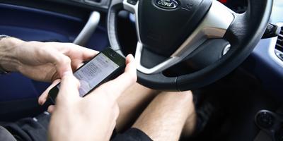 Persoon die sms-berichten typt op zijn smartphone achter het stuur van zijn auto